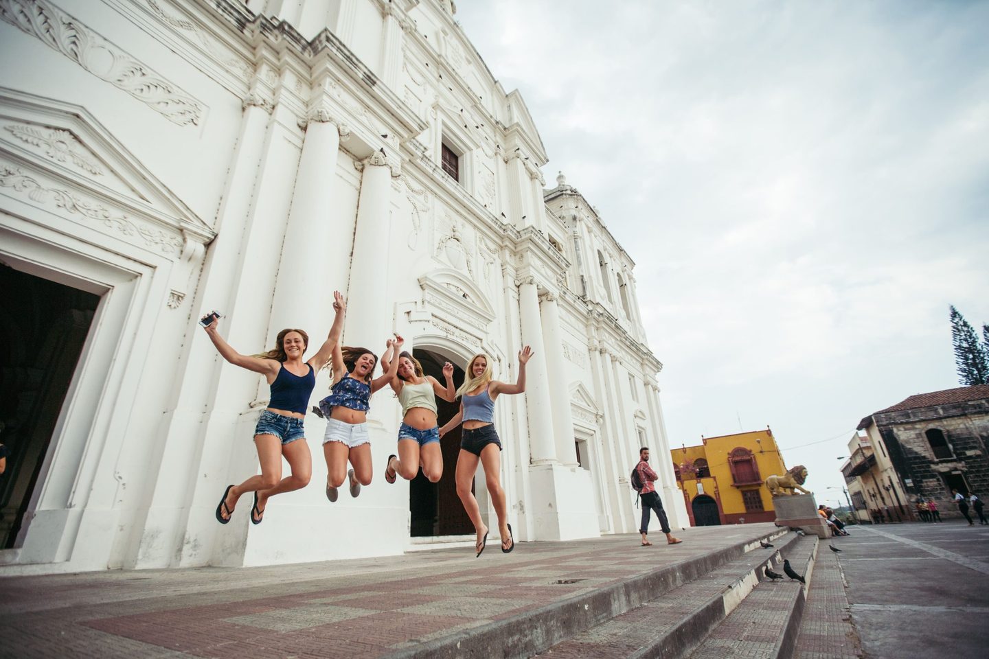 Four travellers jumping in front of the white colonial cathedral in León, Nicaragua