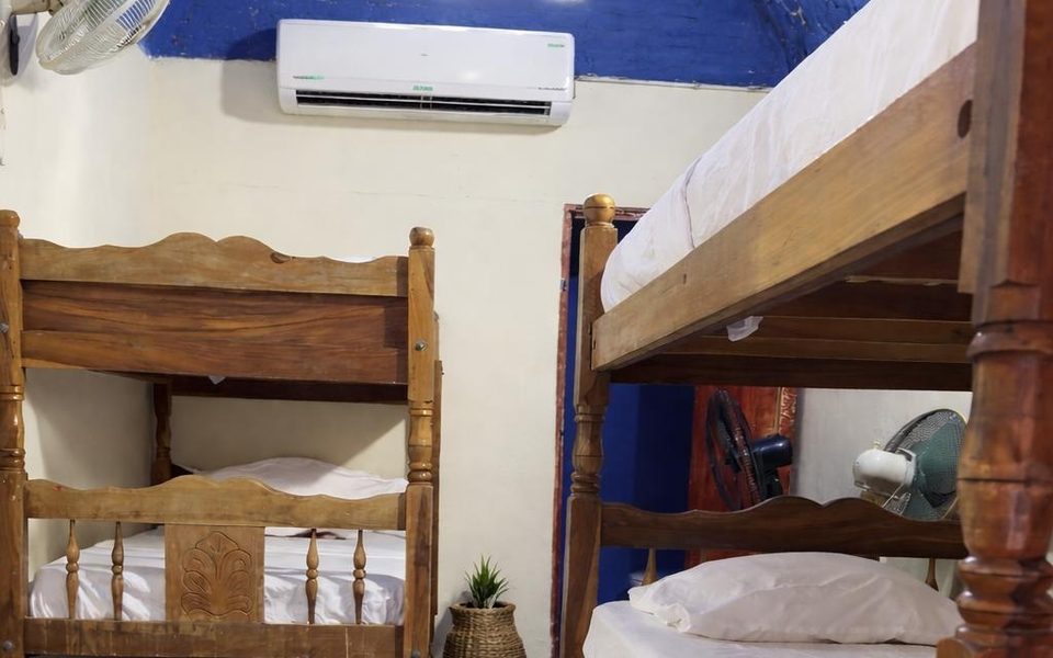 Mixed dorm at Hostal Los Chamos — wooden bunk beds under a blue vaulted ceiling with a wall-mounted A/C unit