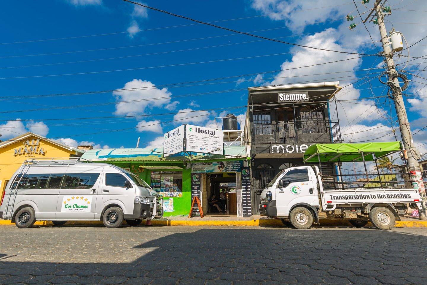 Street frontage of Hostal Los Chamos in San Juan del Sur with the hostel shuttle vans parked outside