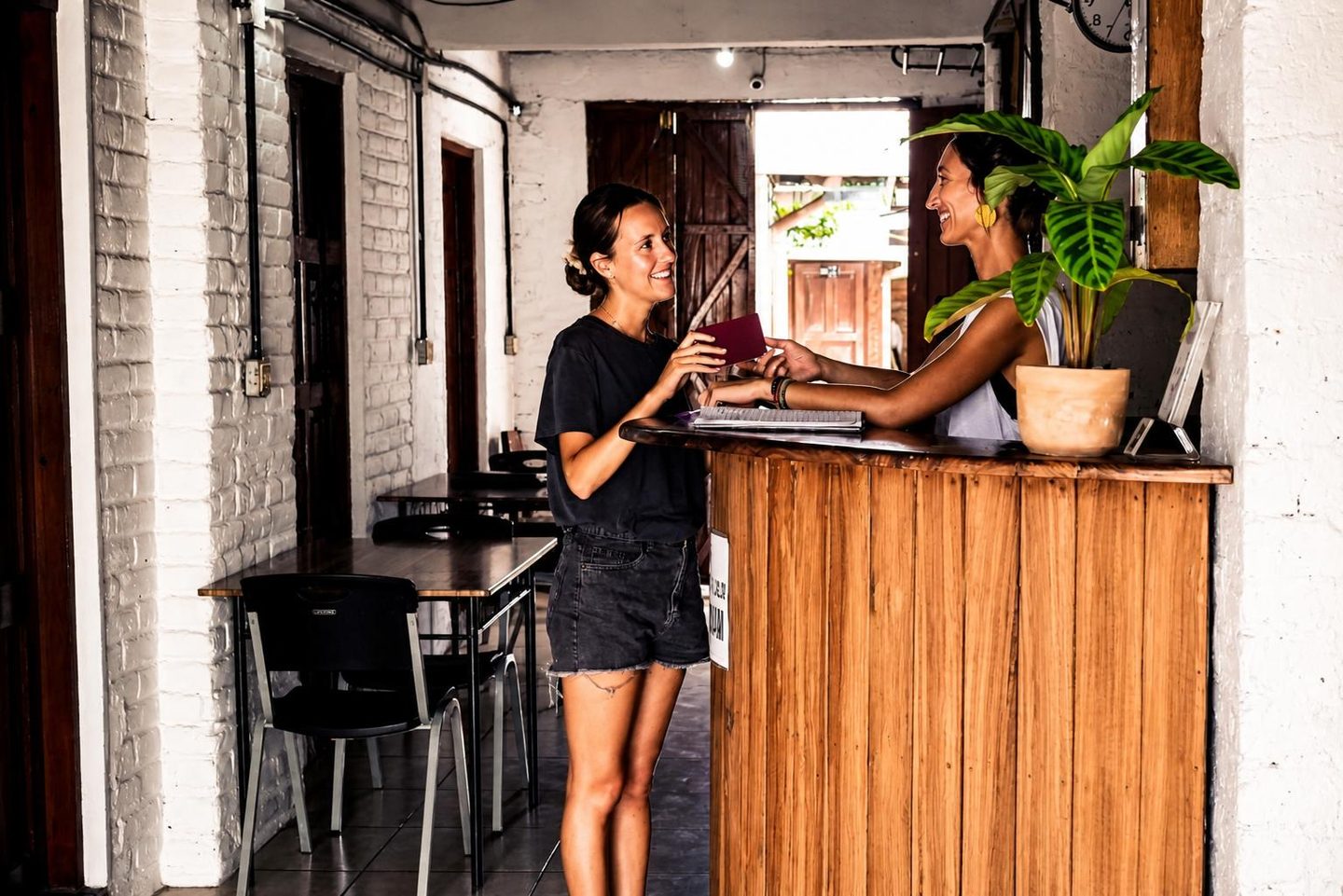 Two travellers laughing at the wooden front desk of Hostal Los Chamos in San Juan del Sur, Nicaragua