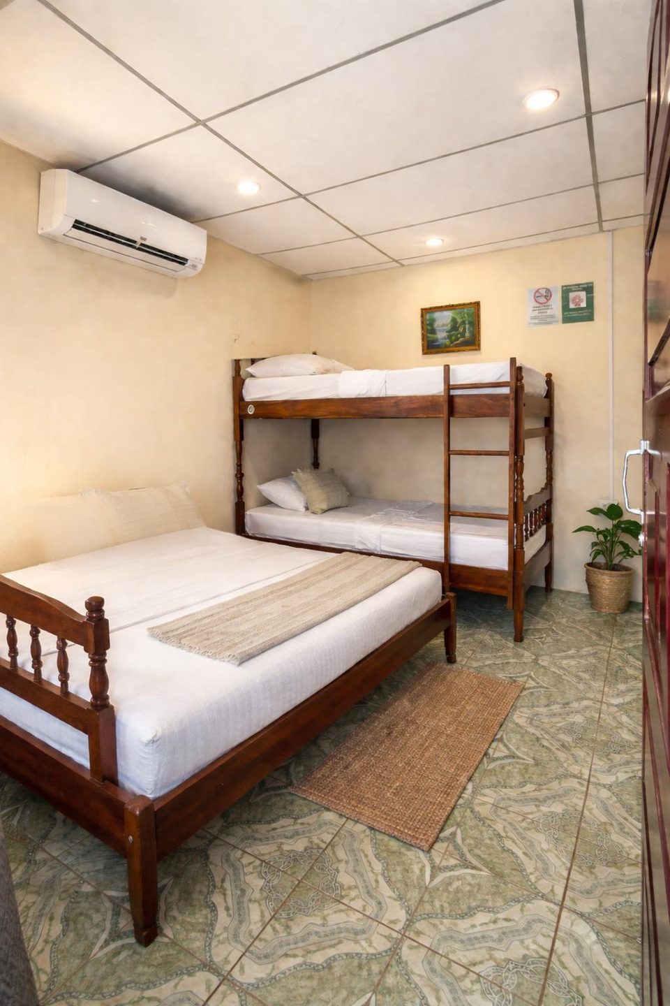Air-conditioned room at Hostal Los Chamos with a double bed and a bunk bed made up with white linen