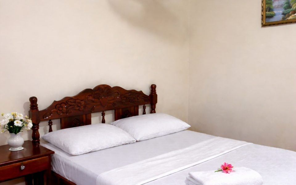 Private double room at Hostal Los Chamos made up with white linen, folded towels with a flower and a bedside table