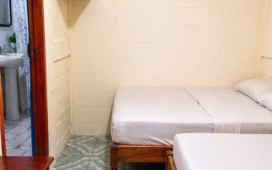 Room at Hostal Los Chamos with two beds made up in white linen and a private bathroom through the doorway