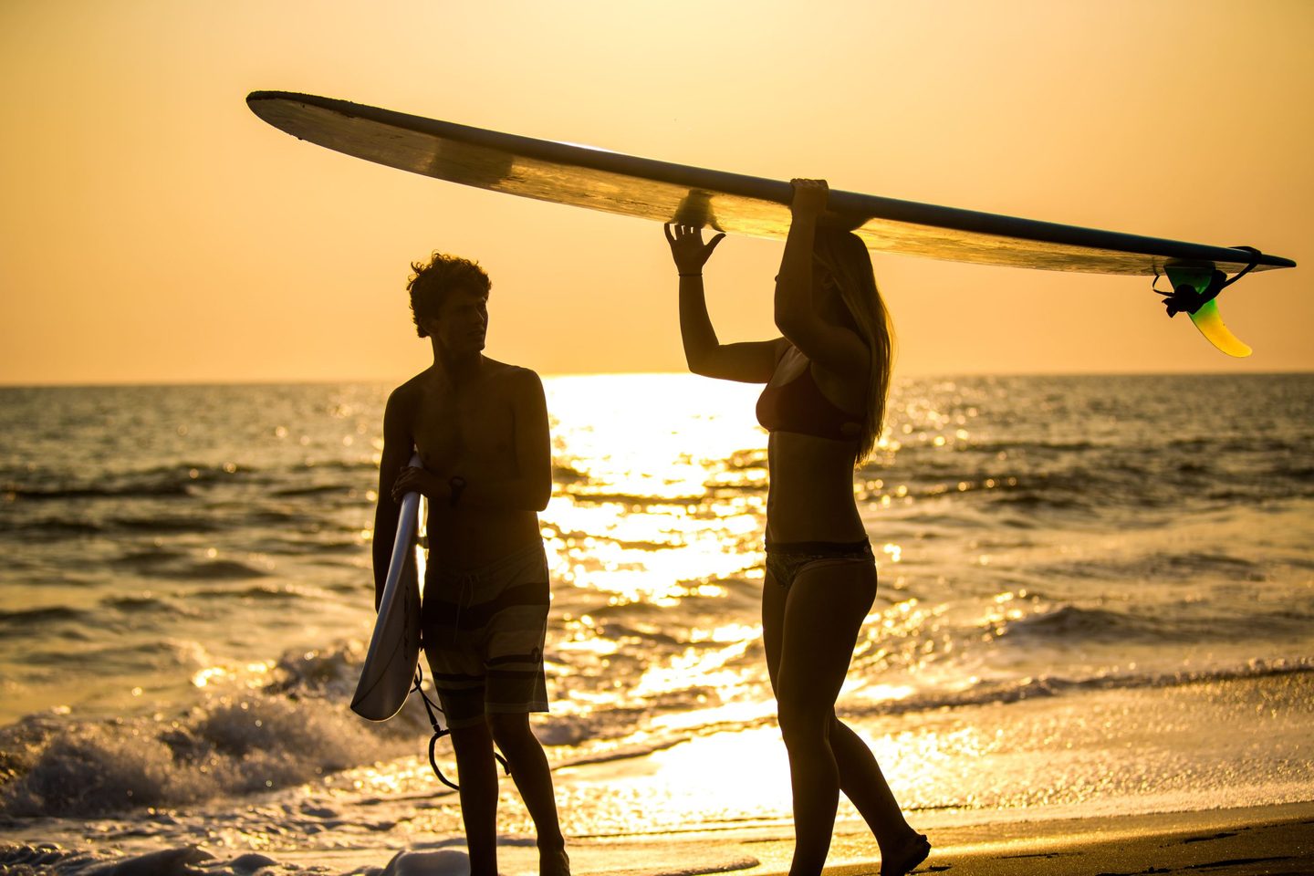 Two surfers walking along the beach at sunset in San Juan del Sur, Nicaragua, carrying their boards